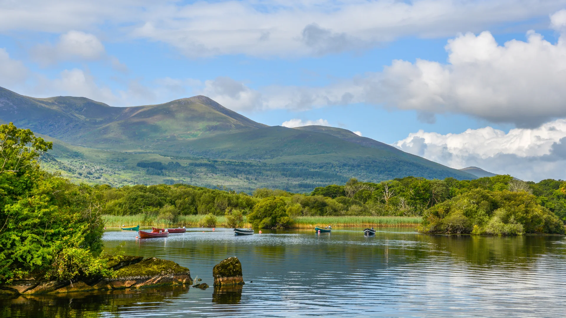 Boats on a lake beneath wooded mountains in County Kerry